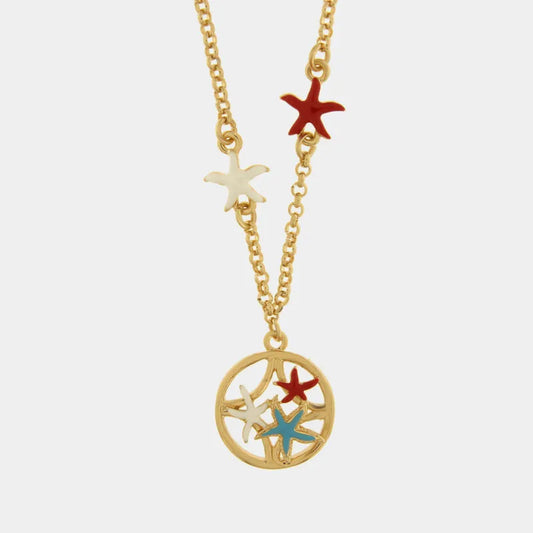 Collana in metallo con finitura dorata del marchio BySimon appartenente alla collezione Fiori di Lava caratterizzata da una catenina a maglia rolo che sostiene un pendente circolare con lavorazione traforata ispirata alle maioliche. Il ciondolo centrale racchiude tre stelle marine tridimensionali smaltate nei colori bianco, rosso e azzurro, mentre lungo la catena sono applicate simmetricamente altre due piccole stelle marine nei colori bianco e rosso. Il gioiello è rifinito con una chiusura a moschettone e 