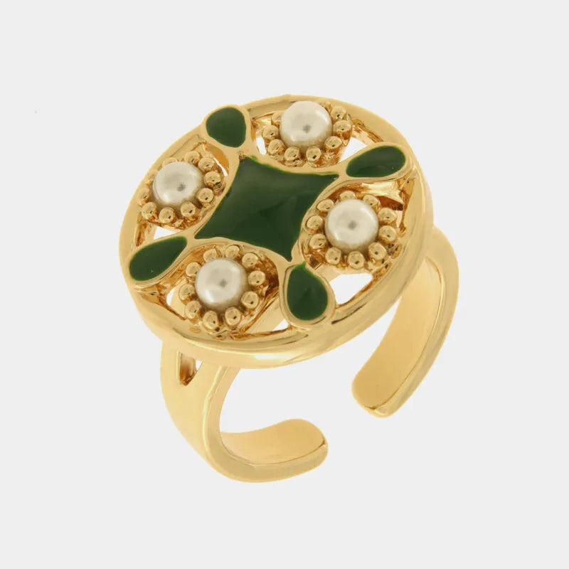 Anello regolabile con finitura dorata del marchio BySimon appartenente alla collezione Fiori di Lava caratterizzato da un importante castone circolare con motivo a maiolica. Il design presenta una croce centrale e decorazioni a goccia smaltate in verde scuro, alternate a quattro perle bianche incastonate all'interno di una cornice di microsfere dorate a rilievo. La struttura dell'anello è lucida e presenta un gambo aperto nella parte inferiore per adattarsi comodamente a diverse misure, rendendolo un access