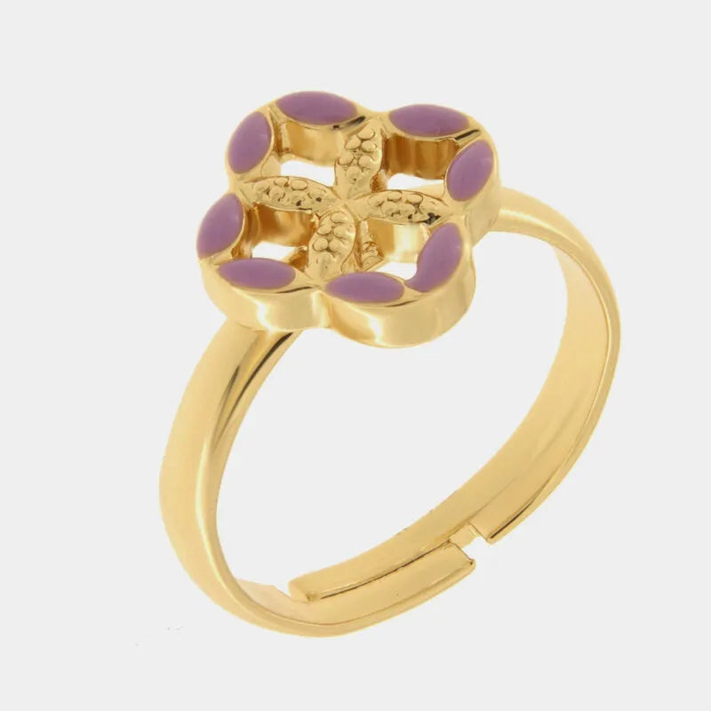 Anello regolabile in metallo con finitura dorata del marchio BySimon appartenente alla collezione Fiori di Lava caratterizzato da un castone centrale a forma di quadrifoglio stilizzato che richiama i decori della Maiolica. Il gioiello è impreziosito da smalto viola applicato sui petali esterni e presenta un motivo a rilievo finemente lavorato nella parte centrale della struttura superiore. La fascia dell'anello è lucida e aperta sul retro per permettere di adattare facilmente la misura al dito, rendendo