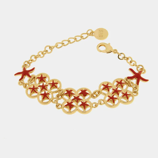 Bracciale in metallo con finitura dorata del marchio BySimon appartenente alla collezione Fiori di Lava caratterizzato da una struttura a doppia catenella nella parte anteriore che sostiene tre elementi circolari traforati a forma di quadrifoglio. Ciascun modulo decorativo è impreziosito da quattro stelle marine in miniatura smaltate in un vivace colore rosso, affiancate da due ulteriori stelle marine rosse poste alle estremità della sezione centrale. Il gioiello è completato da una catenina a maglia rolo, 