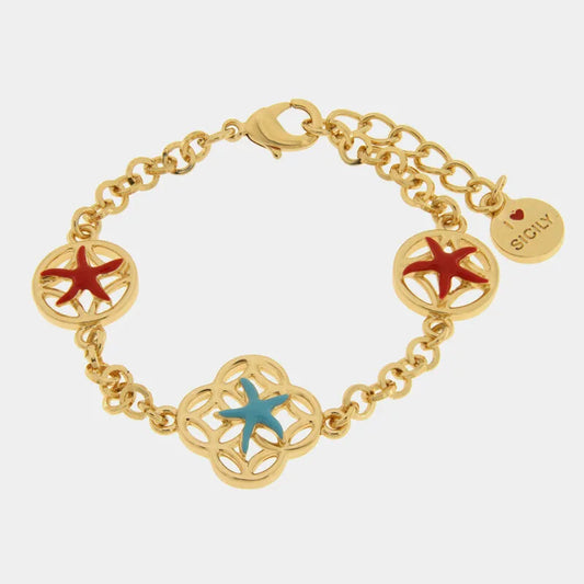 Bracciale in metallo con finitura dorata del marchio BySimon appartenente alla collezione Fiori di Lava caratterizzato da una catenina a maglia rolo impreziosita da tre charms traforati ispirati al mondo marino. Il design presenta un elemento centrale a forma di quadrifoglio con una stella marina smaltata in azzurro, affiancato da due charms circolari laterali decorati con stelle marine di colore rosso. Il gioiello è dotato di una pratica chiusura a moschettone con catenella di estensione e un ciondolo term