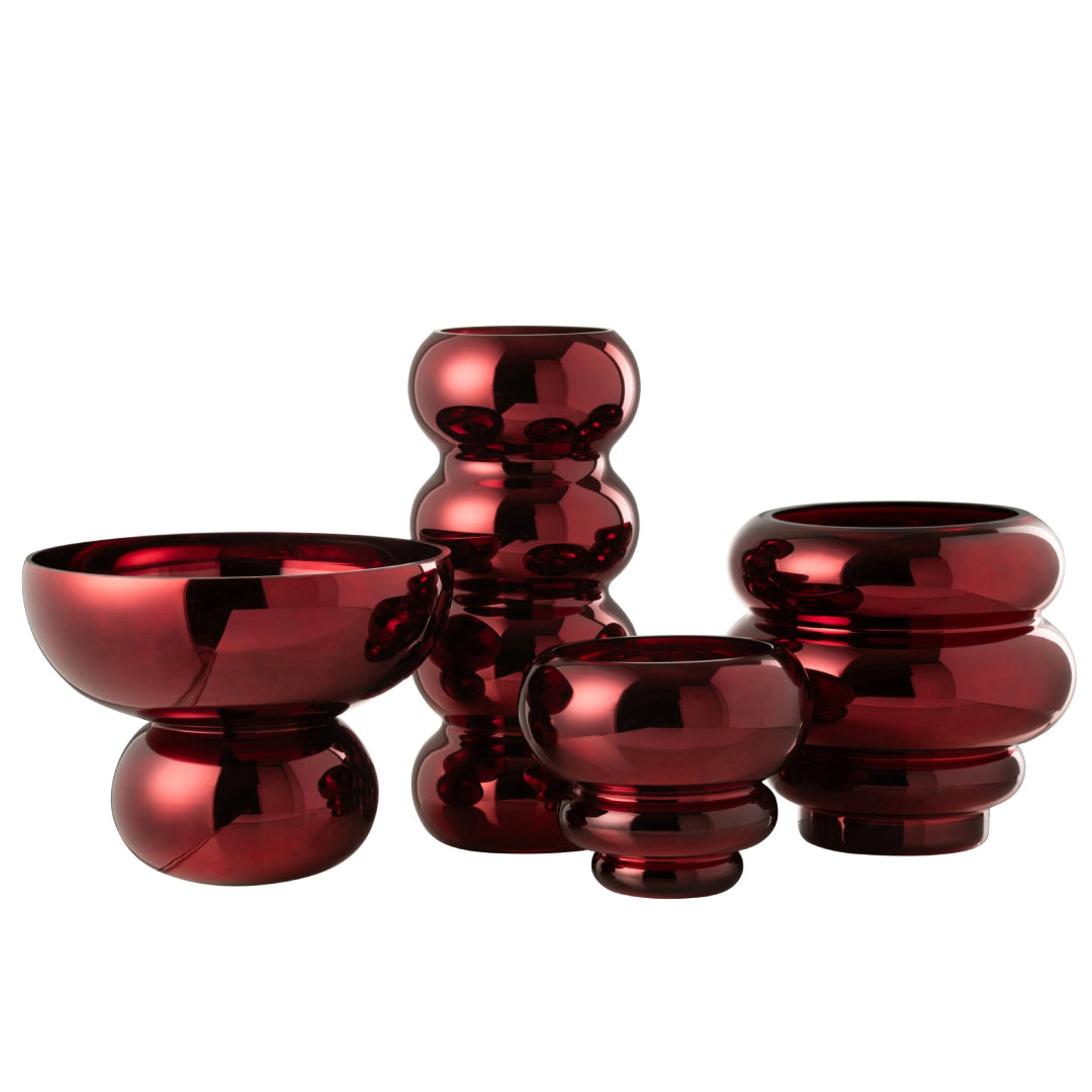 Set di vasi e coppe decorative in vetro lucido color rosso scuro modello Bruco firmato Jolipa, composto da quattro elementi assortiti di diverse forme e altezze con un design moderno a sezioni sferiche e silhouette ondulate. Questa collezione di vasi decorativi e centrotavola di design offre superfici metallizzate a specchio altamente riflettenti, ideali per valorizzare interni contemporanei ed eleganti con composizioni floreali o come raffinati soprammobili.