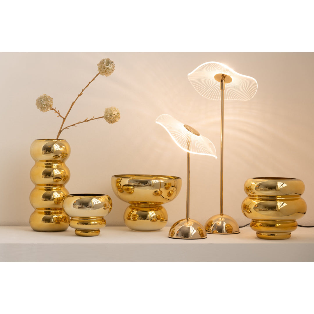Set di portacandele e vasi decorativi assortiti della collezione Julia, abbinati a eleganti lampade da tavolo coordinate, tutti caratterizzati da una lussuosa finitura oro lucida e specchiata. Gli elementi presentano diverse forme bombate, sagomate con design a sfere e cerchi sovrapposti, ideali per creare composizioni scenografiche e infondere un'atmosfera calda, accogliente e di design negli ambienti interni.
