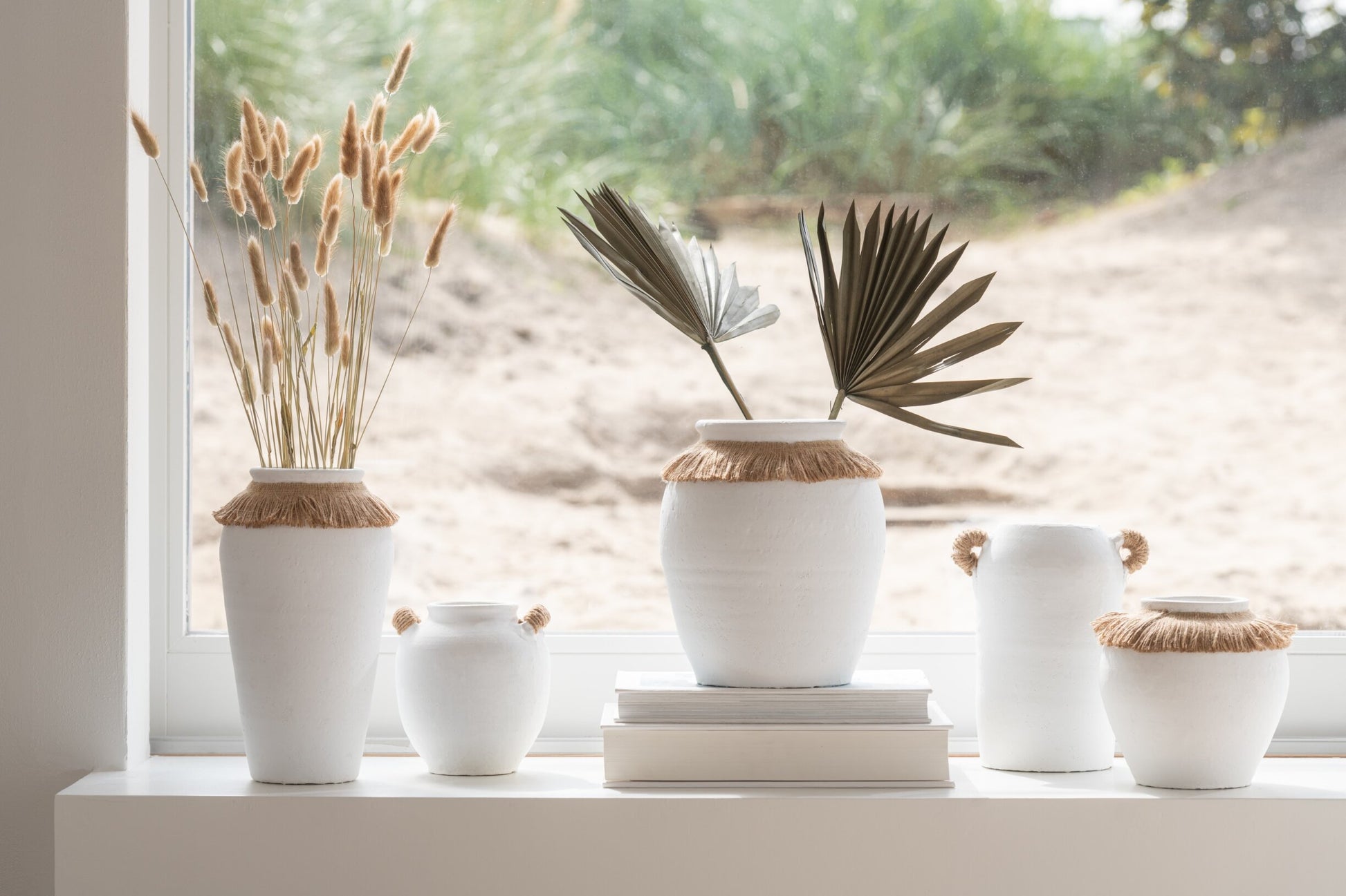Vaso piccolo in ceramica della collezione Ibiza "Oceano Azul" di Jolipa, caratterizzato da una struttura bombata bianca con superficie dall'aspetto materico e naturale. Questo complemento d'arredo è decorato sulla parte superiore da un colletto in juta sfrangiata marrone, ideale per arricchire ambienti in stile boho chic o etnico.