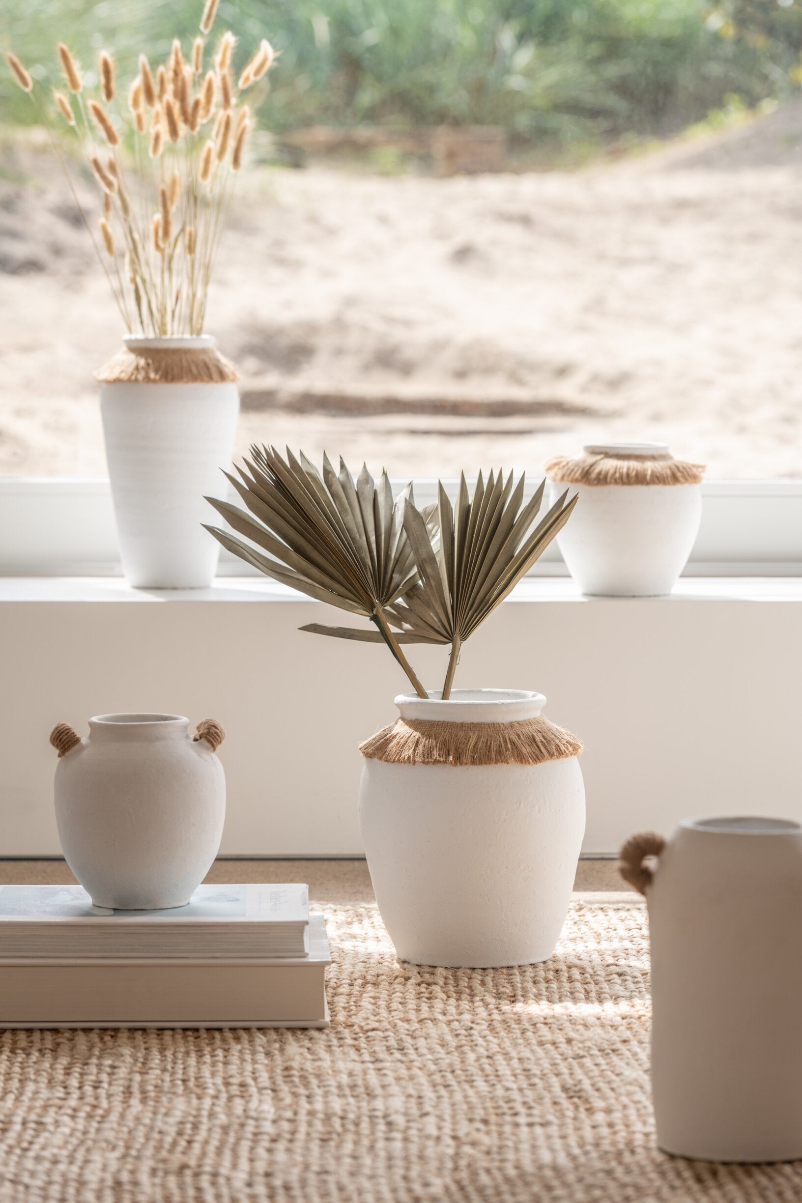 Vaso piccolo in ceramica della collezione Ibiza "Oceano Azul" di Jolipa, caratterizzato da una struttura bombata bianca con superficie dall'aspetto materico e naturale. Questo complemento d'arredo è decorato sulla parte superiore da un colletto in juta sfrangiata marrone, ideale per arricchire ambienti in stile boho chic o etnico.