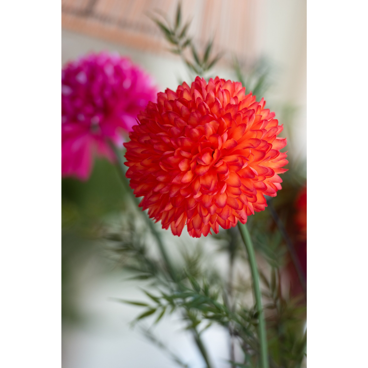 Crisantemo artificiale jolipa con corolla sferica color arancionecomposta da piccoli petali compatti, su lungo stelo verde. Fiore decorativo dall’effetto pompon, ideale per l’home décor e come idea regalo.
