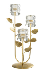 Candeliere decorativo a tre bracci caratterizzato da una struttura metallica dorata con steli disposti a rami ricchi di foglie decorative, che si innalzano da una base circolare satinata. Ognuna delle tre estremità supporta un elegante portacandele in vetro trasparente spesso con lavorazione a rilievo a cerchi sovrapposti, ideale come raffinato centrotavola per creare un'atmosfera calda e accogliente nei tuoi ambienti.