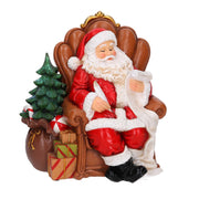 Statuina Vacchetti in resina di Babbo Natale seduto su poltrona mentre scrive la lista dei regali, con albero glitterato e pacchi colorati. Decorazione natalizia dipinta a mano, ideale per l’home décor e come idea regalo.