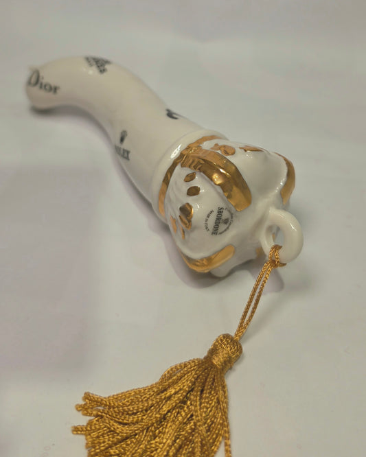 Corno portafortuna in ceramica bianca lucida decorato con loghi fashion neri e completato da una corona regale dorata con nappa in seta oro. Questo elegante oggetto scaramantico di design artigianale rappresenta un complemento d'arredo pop lussuoso e originale, perfetto come idea regalo o decorazione d'interni moderna.