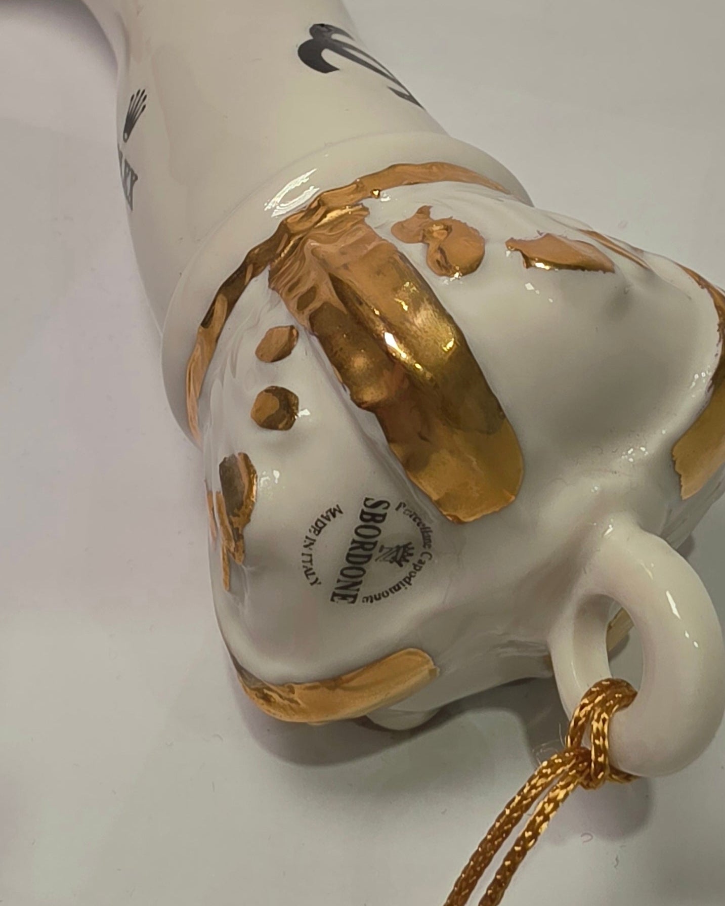 Corno portafortuna in ceramica bianca lucida decorato con loghi fashion neri e completato da una corona regale dorata con nappa in seta oro. Questo elegante oggetto scaramantico di design artigianale rappresenta un complemento d'arredo pop lussuoso e originale, perfetto come idea regalo o decorazione d'interni moderna.