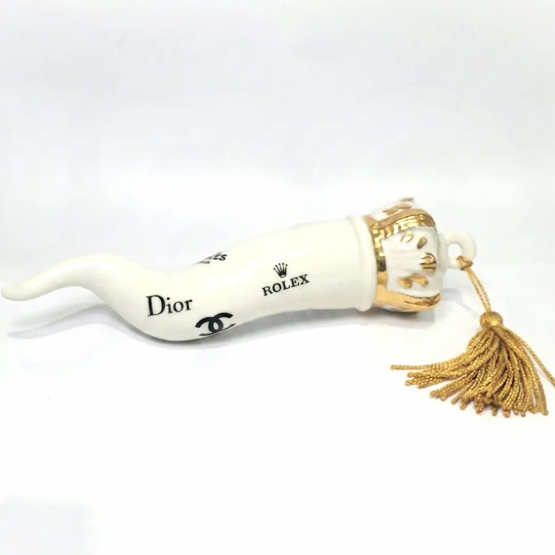 Corno portafortuna in ceramica bianca lucida decorato con loghi fashion neri e completato da una corona regale dorata con nappa in seta oro. Questo elegante oggetto scaramantico di design artigianale rappresenta un complemento d'arredo pop lussuoso e originale, perfetto come idea regalo o decorazione d'interni moderna.