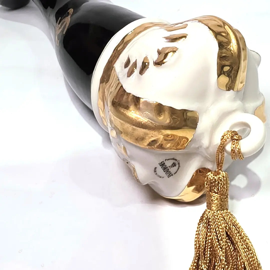 Corno portafortuna in ceramica nera lucida decorato con loghi fashion dorati e completato da una corona regale dorata con nappa in seta oro. Questo elegante oggetto scaramantico di design artigianale rappresenta un complemento d'arredo pop lussuoso e originale, perfetto come idea regalo o decorazione d'interni moderna.