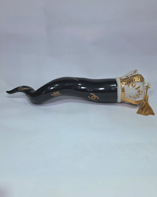 Corno portafortuna in ceramica nera lucida decorato con loghi fashion dorati e completato da una corona regale dorata con nappa in seta oro. Questo elegante oggetto scaramantico di design artigianale rappresenta un complemento d'arredo pop lussuoso e originale, perfetto come idea regalo o decorazione d'interni moderna.