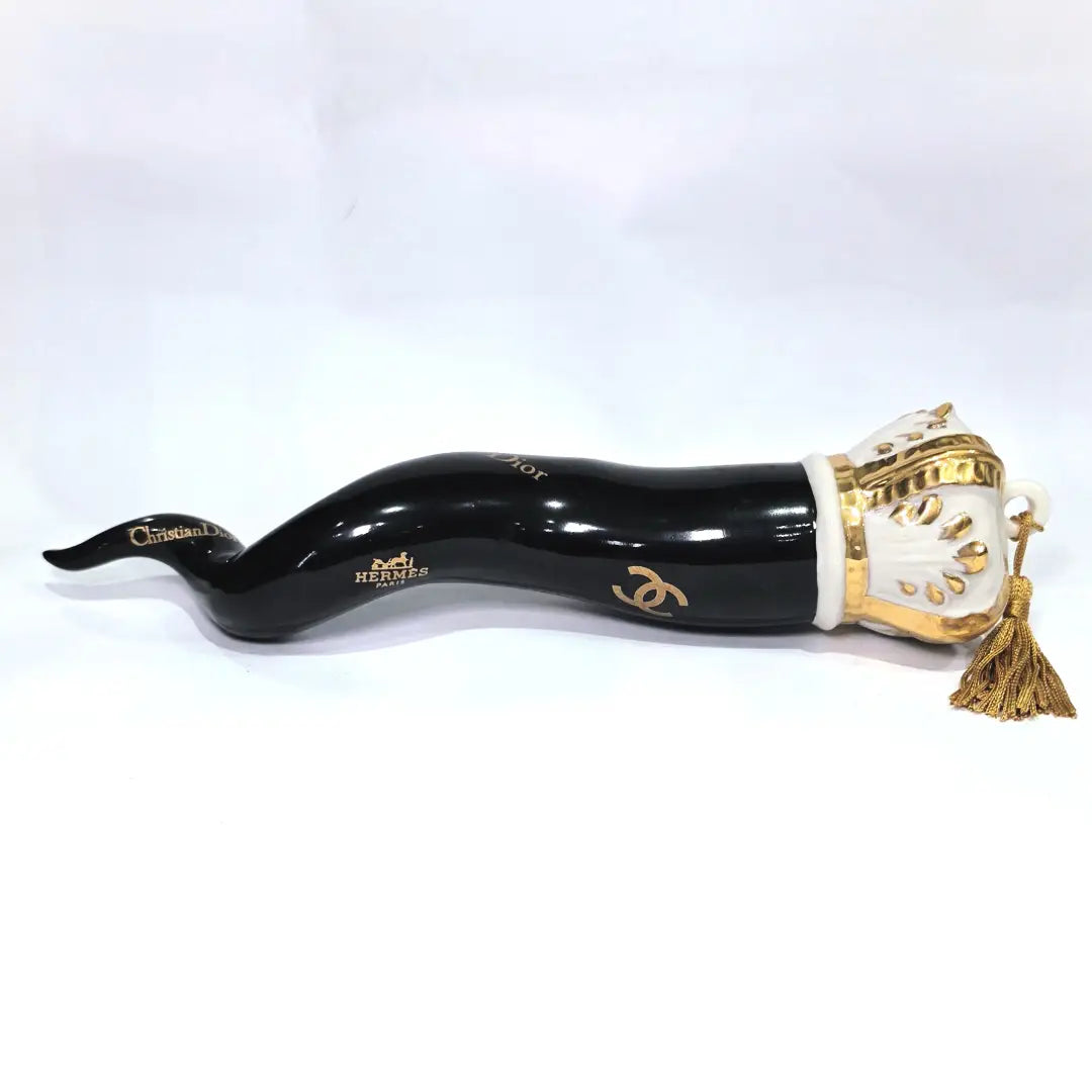 Corno portafortuna in ceramica nera lucida decorato con loghi fashion dorati e completato da una corona regale dorata con nappa in seta oro. Questo elegante oggetto scaramantico di design artigianale rappresenta un complemento d'arredo pop lussuoso e originale, perfetto come idea regalo o decorazione d'interni moderna.