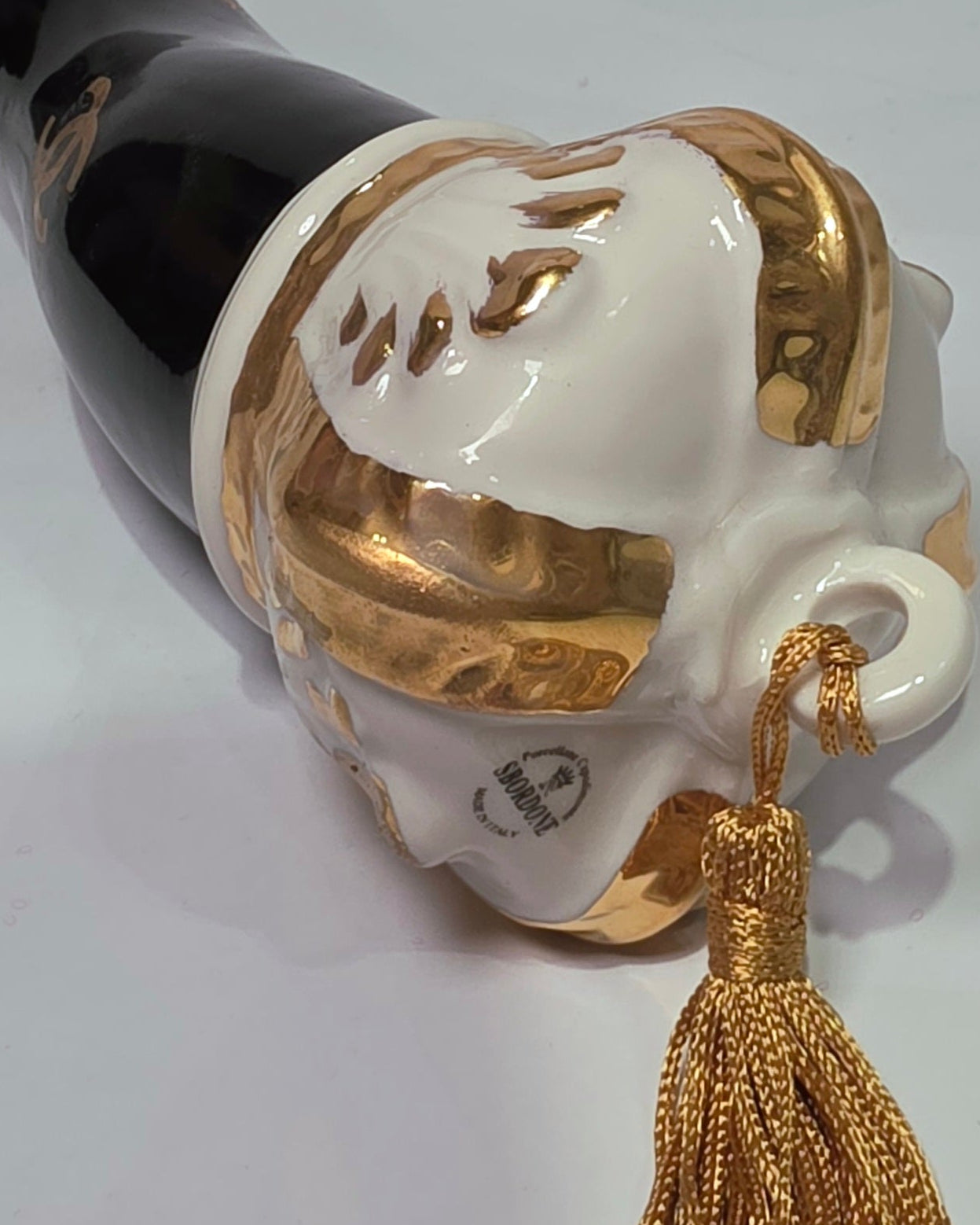 Corno portafortuna in ceramica nera lucida decorato con loghi fashion dorati e completato da una corona regale dorata con nappa in seta oro. Questo elegante oggetto scaramantico di design artigianale rappresenta un complemento d'arredo pop lussuoso e originale, perfetto come idea regalo o decorazione d'interni moderna.