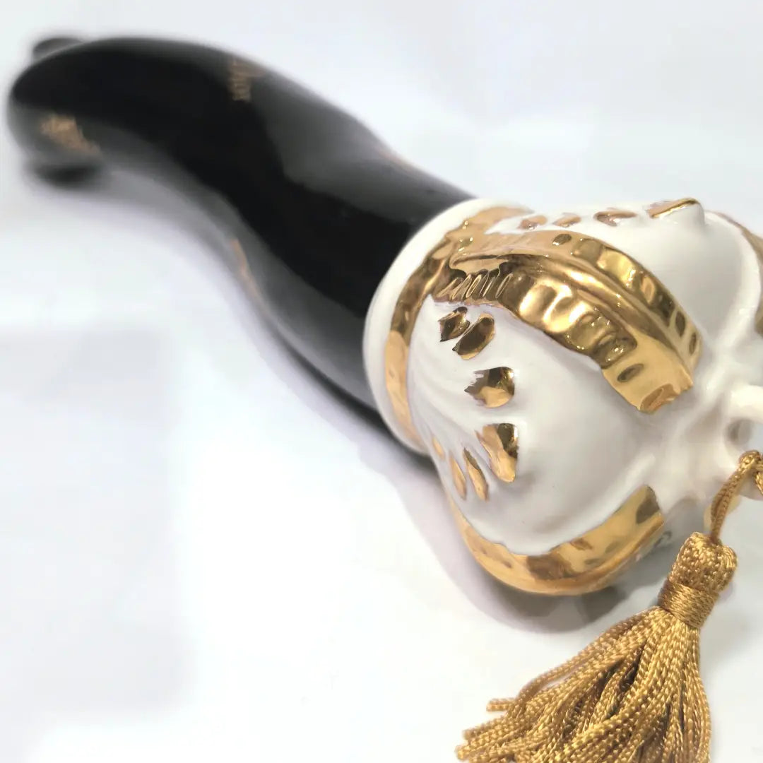 Corno portafortuna in ceramica nera lucida decorato con loghi fashion dorati e completato da una corona regale dorata con nappa in seta oro. Questo elegante oggetto scaramantico di design artigianale rappresenta un complemento d'arredo pop lussuoso e originale, perfetto come idea regalo o decorazione d'interni moderna.