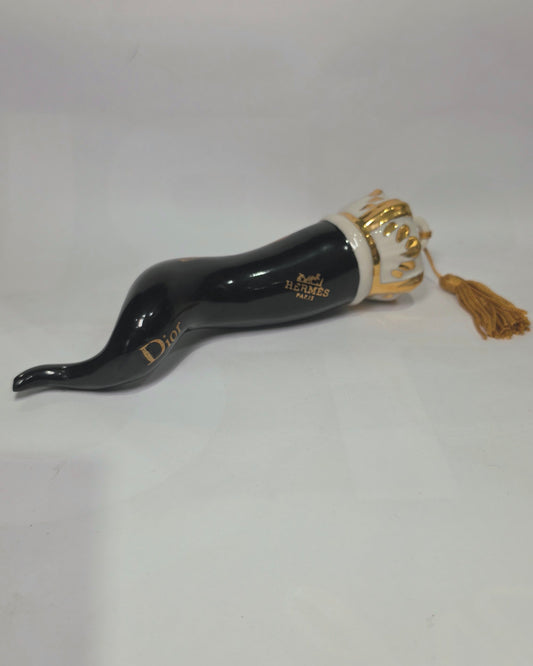 Corno portafortuna in ceramica nera lucida decorato con loghi fashion dorati e completato da una corona regale dorata con nappa in seta oro. Questo elegante oggetto scaramantico di design artigianale rappresenta un complemento d'arredo pop lussuoso e originale, perfetto come idea regalo o decorazione d'interni moderna.