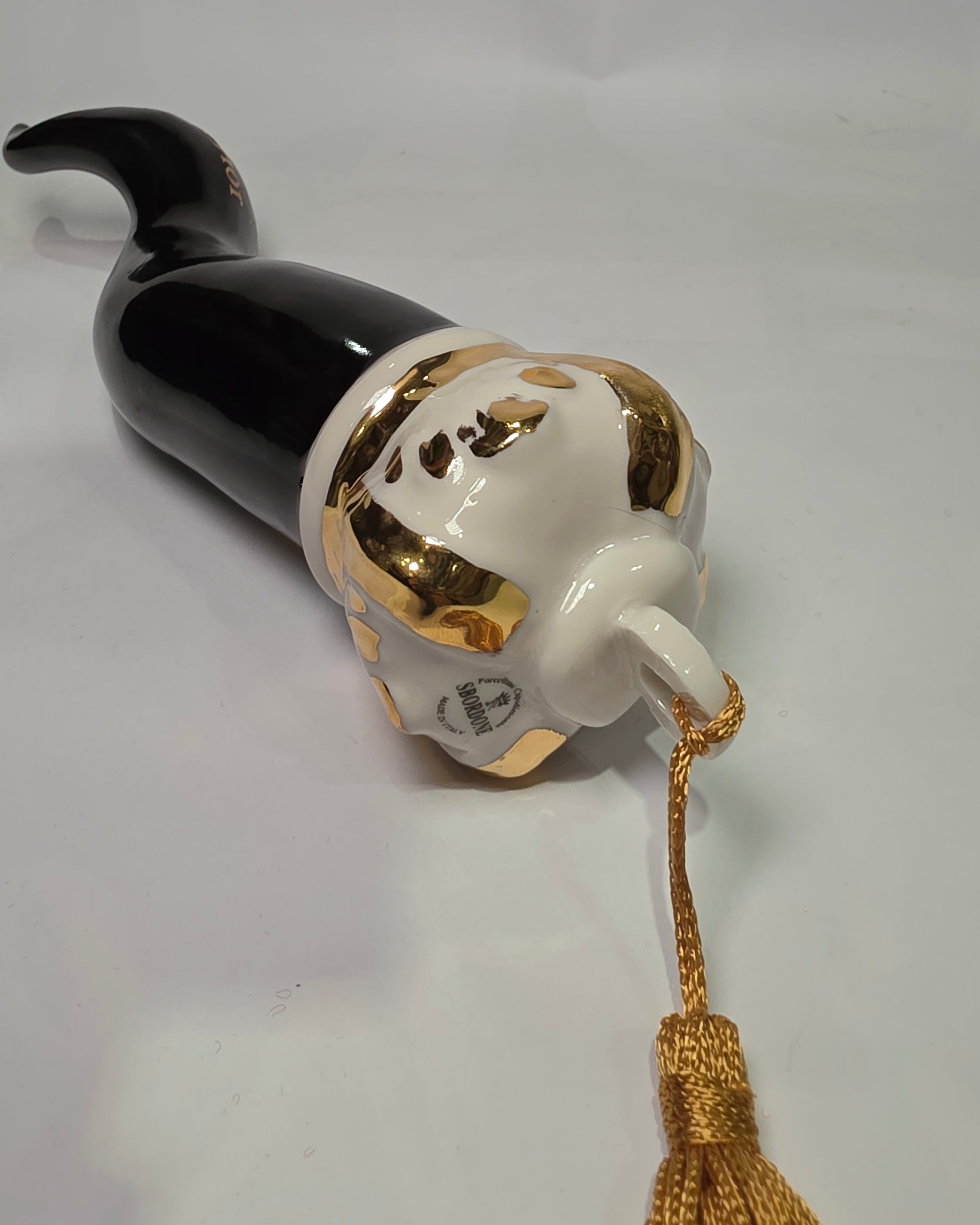 Corno portafortuna in ceramica nera lucida decorato con loghi fashion dorati e completato da una corona regale dorata con nappa in seta oro. Questo elegante oggetto scaramantico di design artigianale rappresenta un complemento d'arredo pop lussuoso e originale, perfetto come idea regalo o decorazione d'interni moderna.
