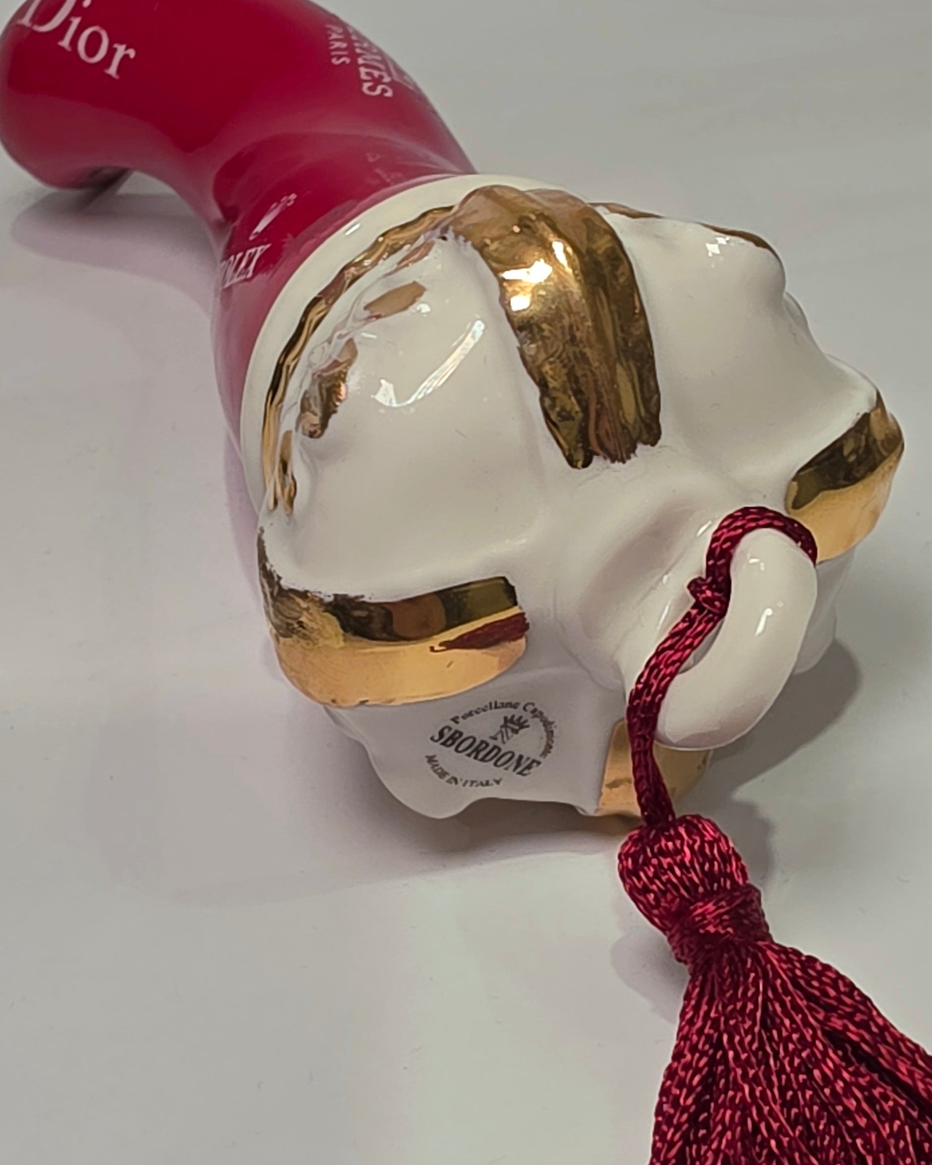 Corno portafortuna in ceramica rossa lucida decorato con loghi fashion bianchi e completato da una corona regale dorata con nappa in seta rossa. Questo elegante oggetto scaramantico di design artigianale rappresenta un complemento d'arredo pop lussuoso e originale, perfetto come idea regalo o decorazione d'interni moderna.