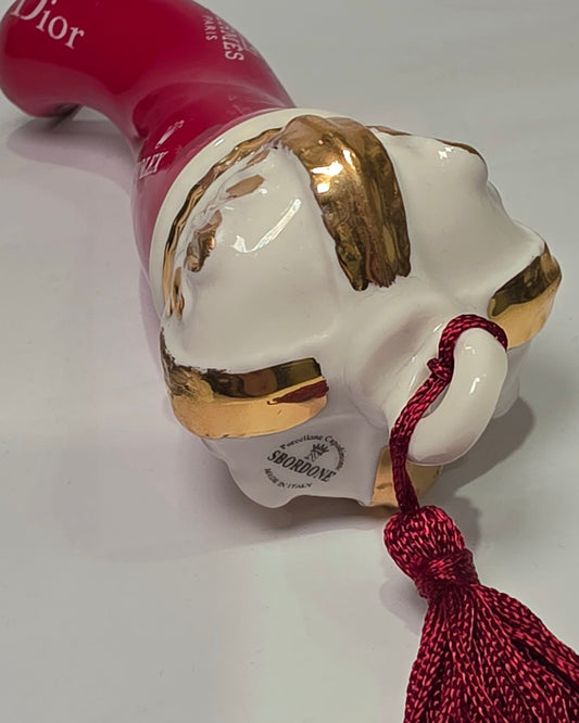 Corno portafortuna in ceramica rossa lucida decorato con loghi fashion bianchi e completato da una corona regale dorata con nappa in seta rossa. Questo elegante oggetto scaramantico di design artigianale rappresenta un complemento d'arredo pop lussuoso e originale, perfetto come idea regalo o decorazione d'interni moderna.