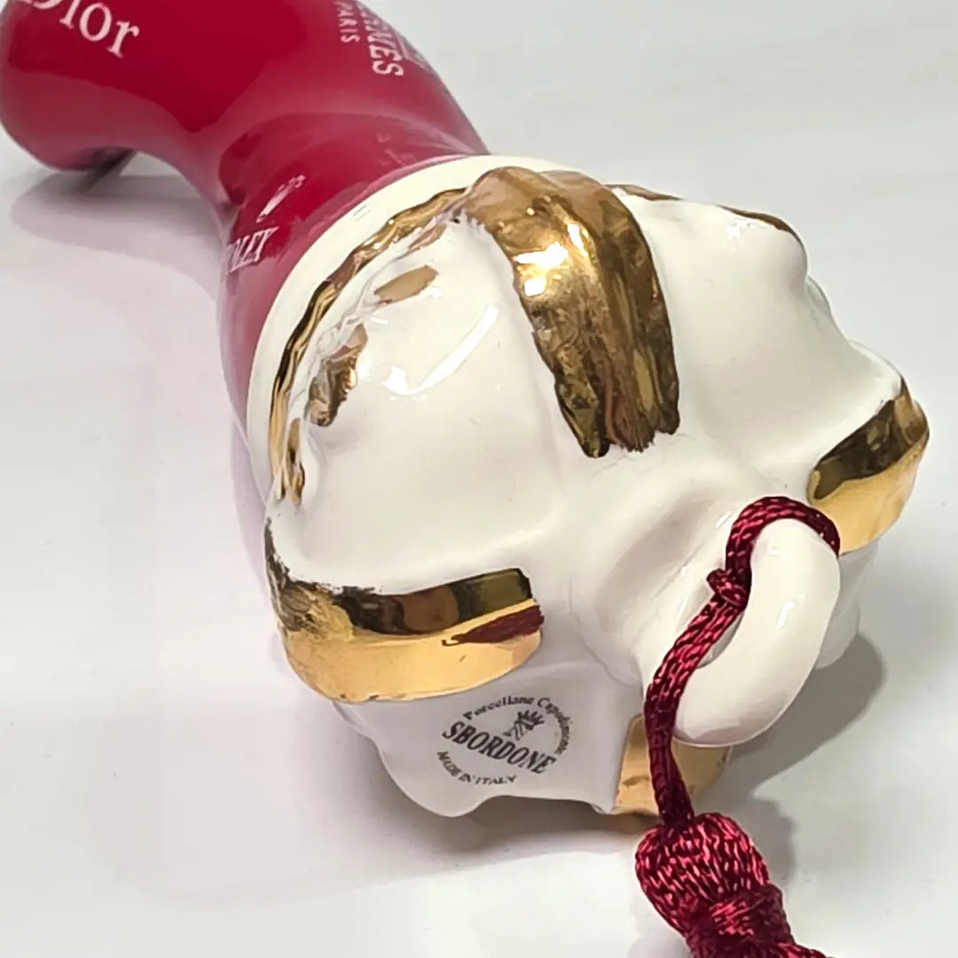 Corno portafortuna in ceramica rossa lucida decorato con loghi fashion bianchi e completato da una corona regale dorata con nappa in seta rossa. Questo elegante oggetto scaramantico di design artigianale rappresenta un complemento d'arredo pop lussuoso e originale, perfetto come idea regalo o decorazione d'interni moderna.