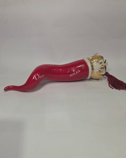 Corno portafortuna in ceramica rossa lucida decorato con loghi fashion bianchi e completato da una corona regale dorata con nappa in seta rossa. Questo elegante oggetto scaramantico di design artigianale rappresenta un complemento d'arredo pop lussuoso e originale, perfetto come idea regalo o decorazione d'interni moderna.