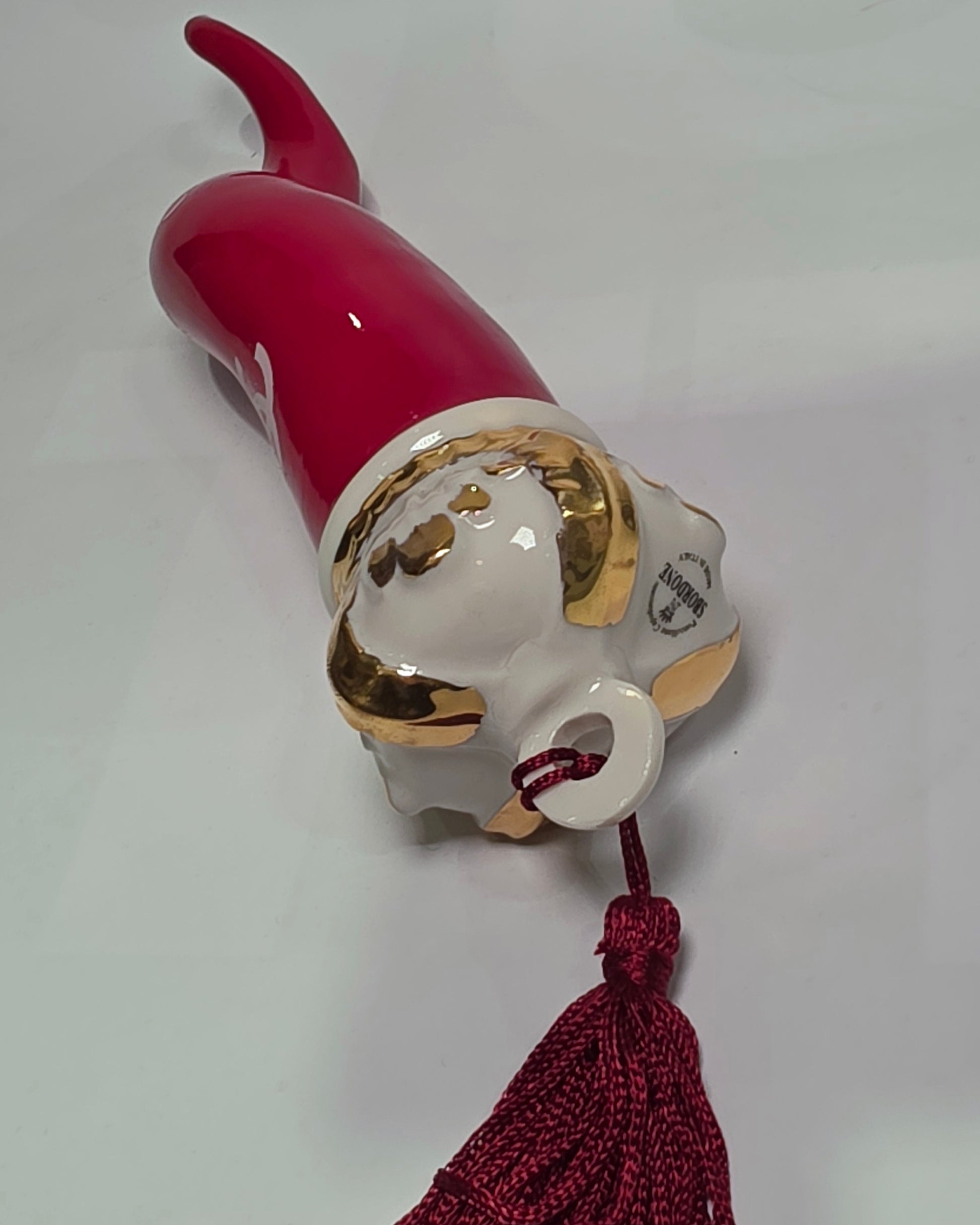 Corno portafortuna in ceramica rossa lucida decorato con loghi fashion bianchi e completato da una corona regale dorata con nappa in seta rossa. Questo elegante oggetto scaramantico di design artigianale rappresenta un complemento d'arredo pop lussuoso e originale, perfetto come idea regalo o decorazione d'interni moderna.