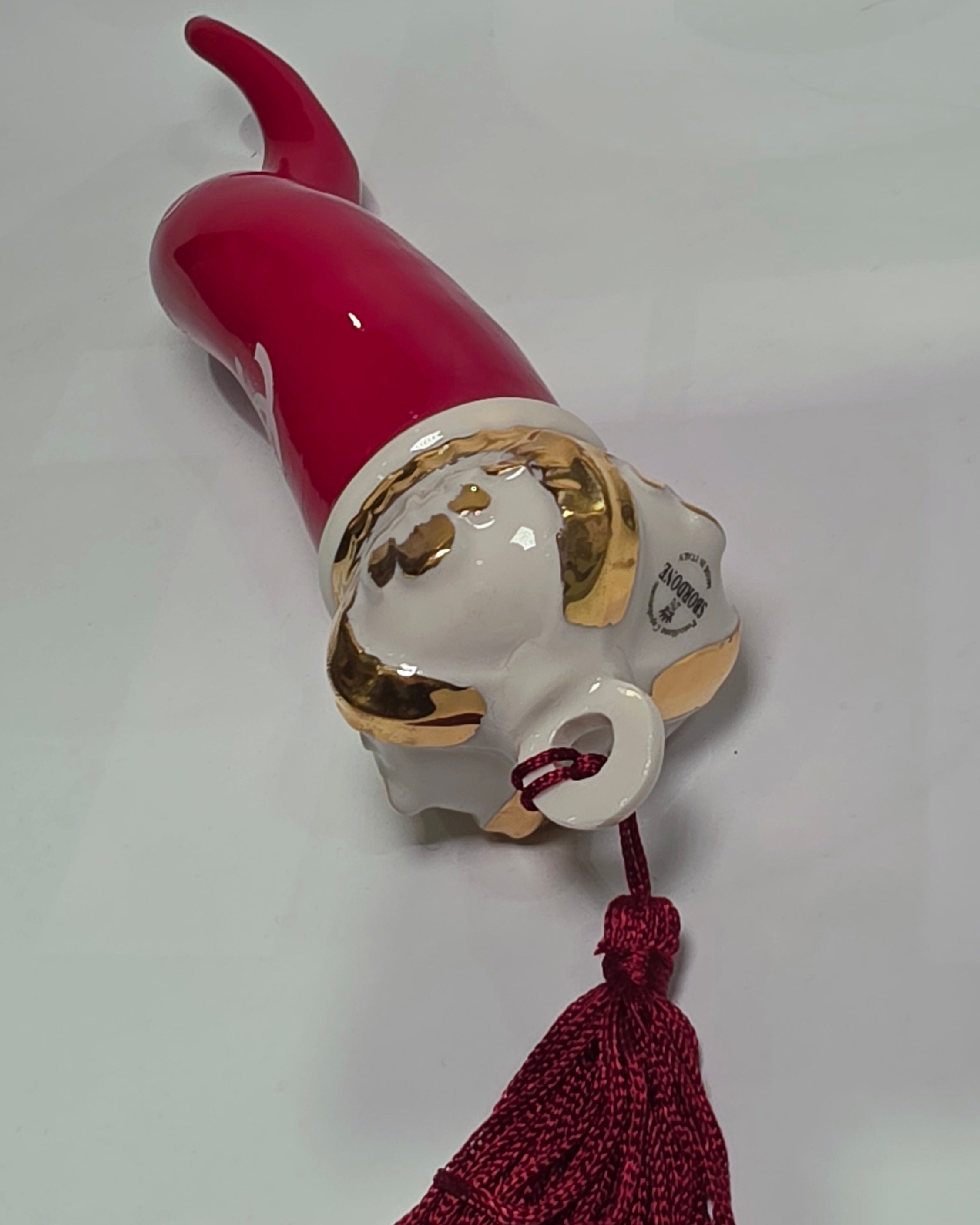 Corno portafortuna in ceramica rossa lucida decorato con loghi fashion bianchi e completato da una corona regale dorata con nappa in seta rossa. Questo elegante oggetto scaramantico di design artigianale rappresenta un complemento d'arredo pop lussuoso e originale, perfetto come idea regalo o decorazione d'interni moderna.