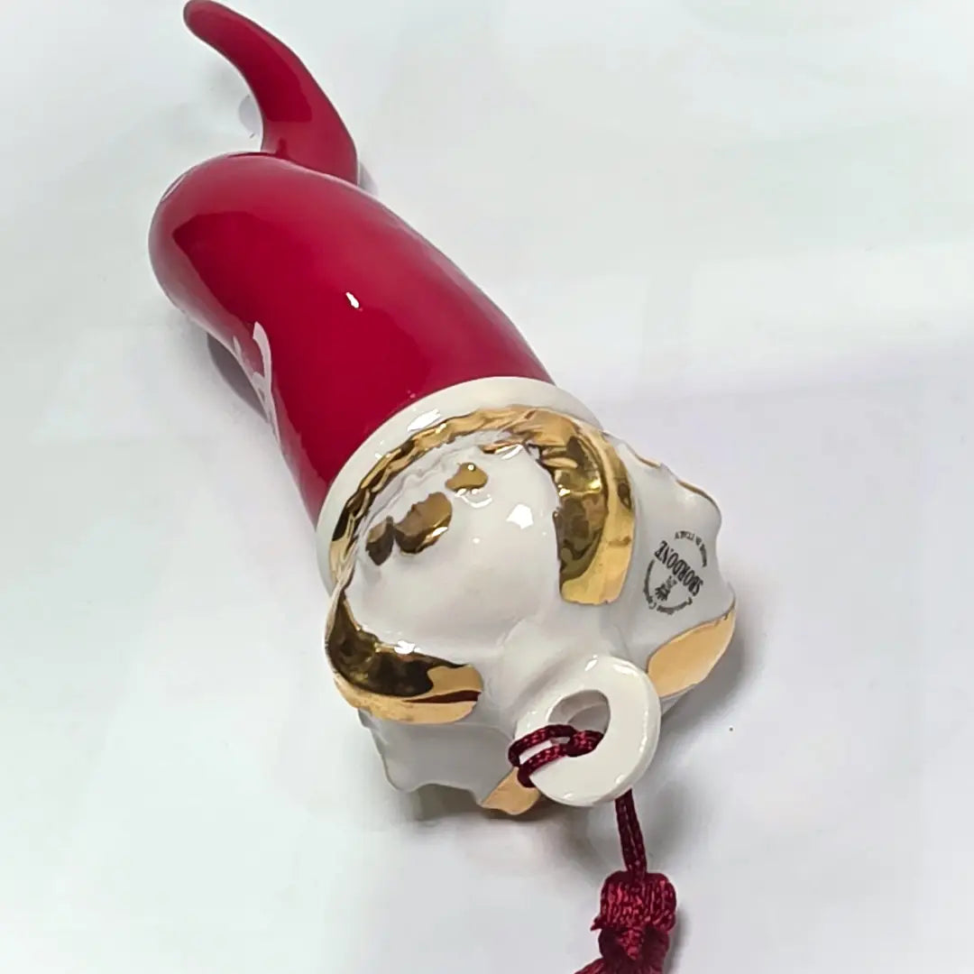 Corno portafortuna in ceramica rossa lucida decorato con loghi fashion bianchi e completato da una corona regale dorata con nappa in seta rossa. Questo elegante oggetto scaramantico di design artigianale rappresenta un complemento d'arredo pop lussuoso e originale, perfetto come idea regalo o decorazione d'interni moderna.