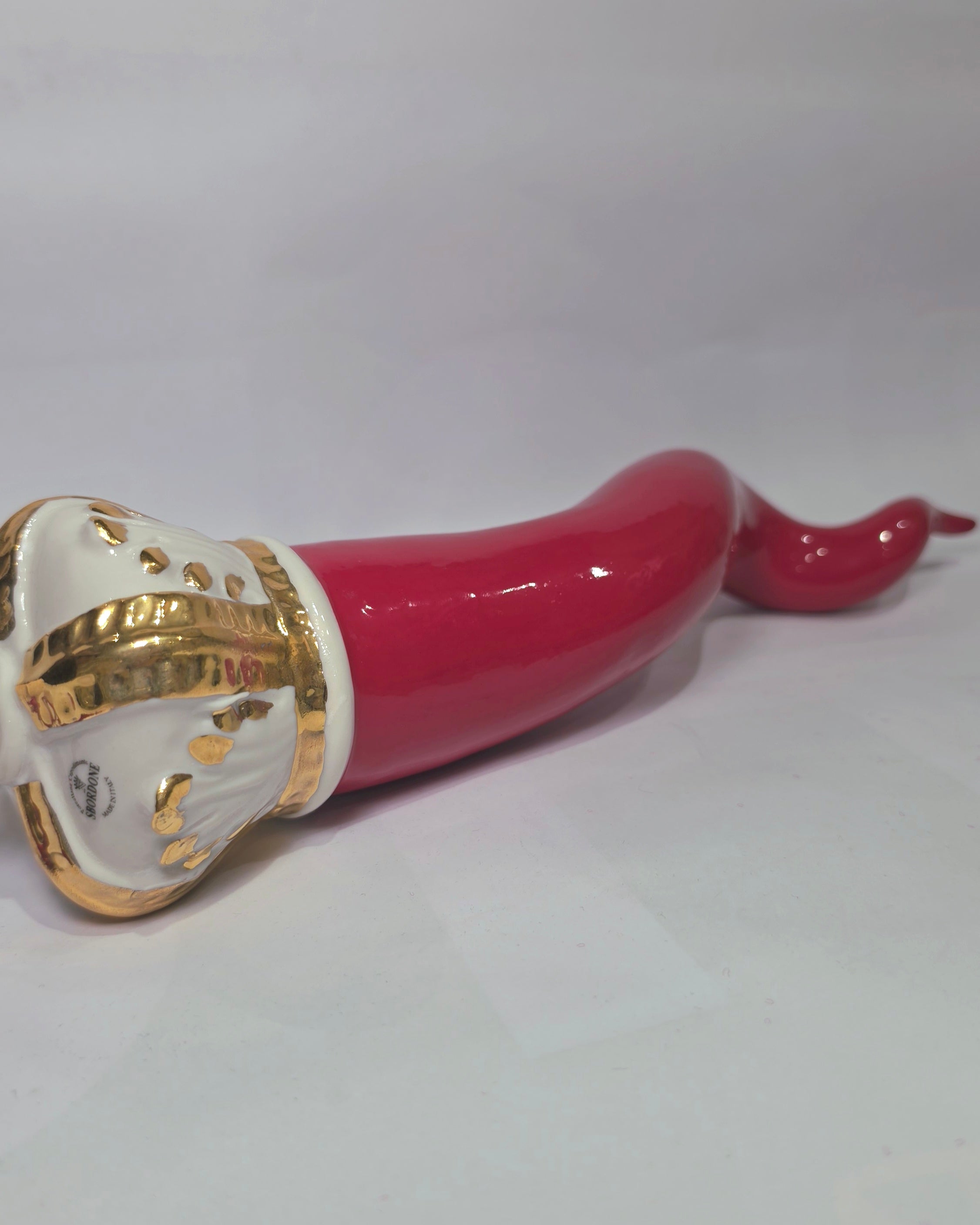 Corno portafortuna in ceramica rossa lucida caratterizzato da una corona regale bianca con decorazioni dorate e una nappa in tessuto rosso coordinata. Questo raffinato amuleto scaramantico dal design artigianale è un complemento d'arredo perfetto per decorare la casa con stile e tradizione.