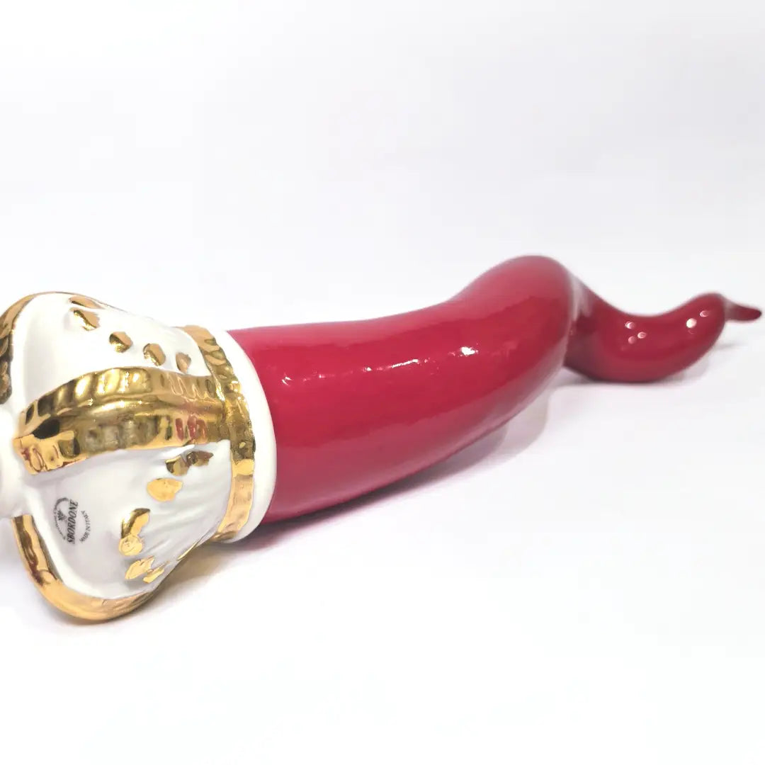 Corno portafortuna in ceramica rossa lucida caratterizzato da una corona regale bianca con decorazioni dorate e una nappa in tessuto rosso coordinata. Questo raffinato amuleto scaramantico dal design artigianale è un complemento d'arredo perfetto per decorare la casa con stile e tradizione.