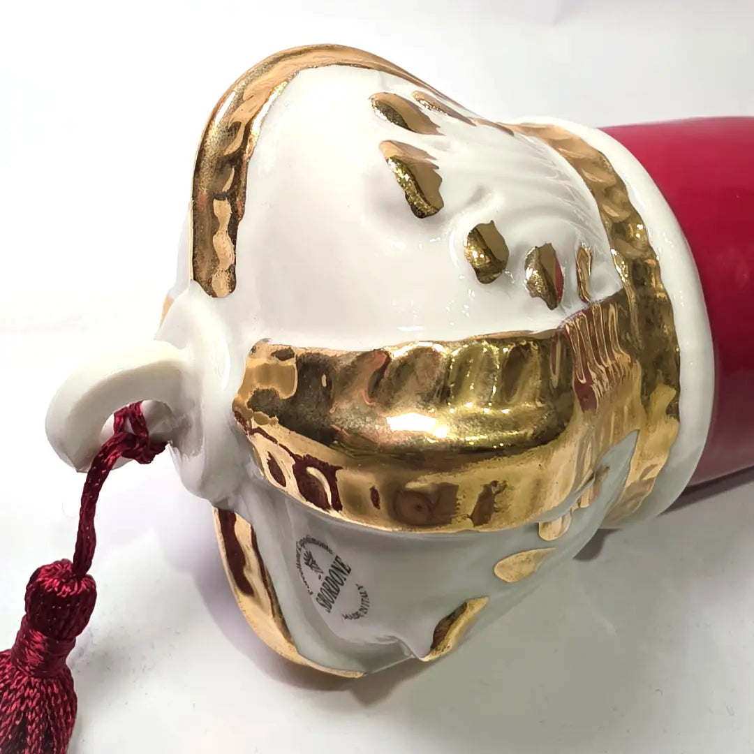 Corno portafortuna in ceramica rossa lucida caratterizzato da una corona regale bianca con decorazioni dorate e una nappa in tessuto rosso coordinata. Questo raffinato amuleto scaramantico dal design artigianale è un complemento d'arredo perfetto per decorare la casa con stile e tradizione.