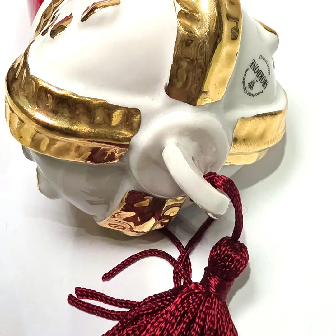 Corno portafortuna in ceramica rossa lucida caratterizzato da una corona regale bianca con decorazioni dorate e una nappa in tessuto rosso coordinata. Questo raffinato amuleto scaramantico dal design artigianale è un complemento d'arredo perfetto per decorare la casa con stile e tradizione.
