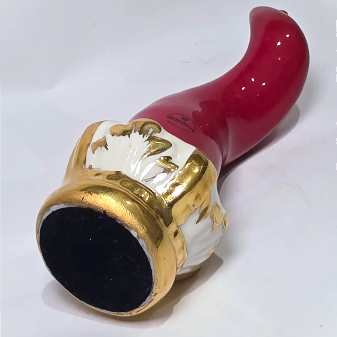 Corno portafortuna Regale in ceramica rossa lucida montato su una raffinata base d'appoggio bianca con eleganti venature e finiture dorate. Questo oggetto scaramantico di design artigianale, sormontato da una corona oro, rappresenta un complemento d'arredo esclusivo ideale per impreziosire interni moderni o classici.
