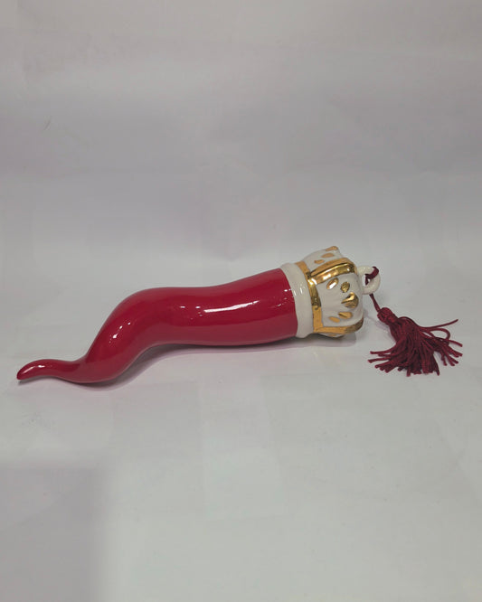 Corno portafortuna in ceramica rossa lucida caratterizzato da una corona regale bianca con decorazioni dorate e una nappa in tessuto rosso coordinata. Questo raffinato amuleto scaramantico dal design artigianale è un complemento d'arredo perfetto per decorare la casa con stile e tradizione.
