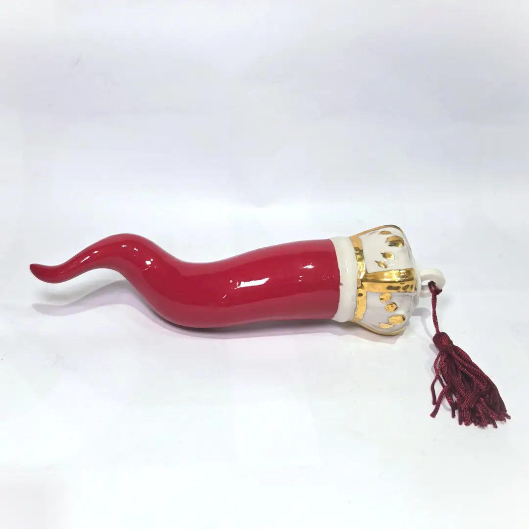 Corno portafortuna in ceramica rossa lucida caratterizzato da una corona regale bianca con decorazioni dorate e una nappa in tessuto rosso coordinata. Questo raffinato amuleto scaramantico dal design artigianale è un complemento d'arredo perfetto per decorare la casa con stile e tradizione.