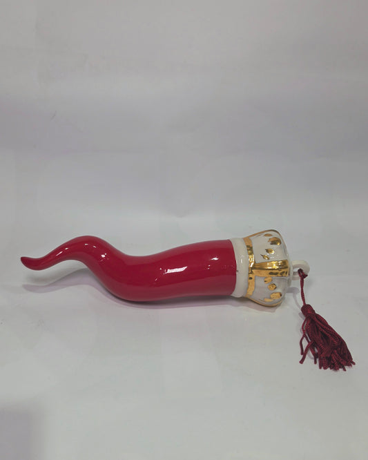 Corno portafortuna in ceramica rossa lucida caratterizzato da una corona regale bianca con decorazioni dorate e una nappa in tessuto rosso coordinata. Questo raffinato amuleto scaramantico dal design artigianale è un complemento d'arredo perfetto per decorare la casa con stile e tradizione.