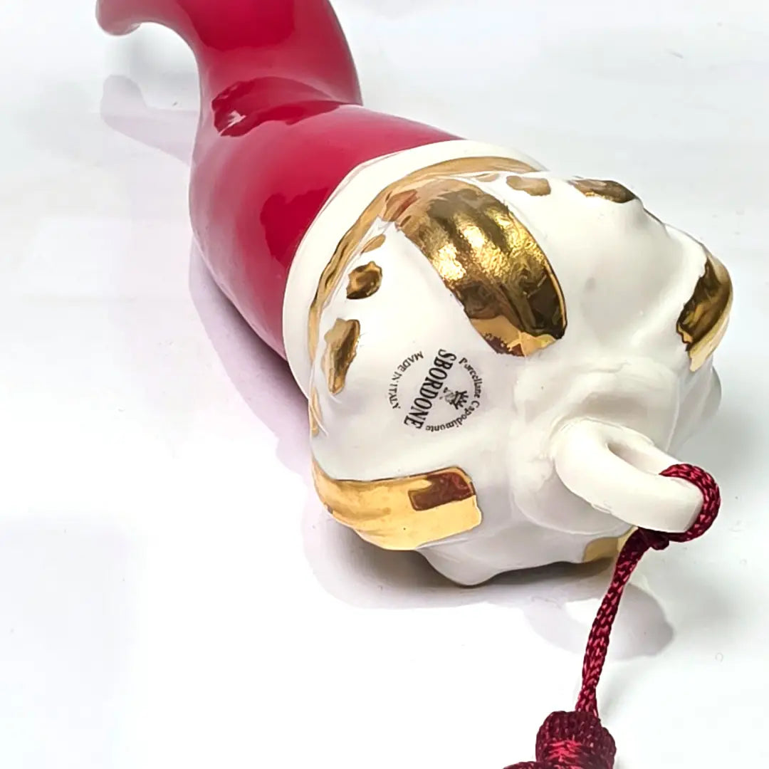 Corno portafortuna in ceramica rossa lucida caratterizzato da una corona regale bianca con decorazioni dorate e una nappa in tessuto rosso coordinata. Questo raffinato amuleto scaramantico dal design artigianale è un complemento d'arredo perfetto per decorare la casa con stile e tradizione.