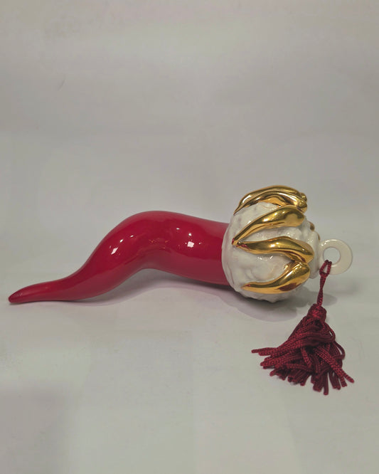 Corno portafortuna in ceramica rossa lucida di manifattura artigianale, caratterizzato da una punta ricurva e una corona regale dorata posta sulla sommità. Questo amuleto scaramantico dal design classico è un complemento d'arredo elegante, ideale come regalo di buon augurio o per decorare ambienti con un tocco di tradizione mediterranea.