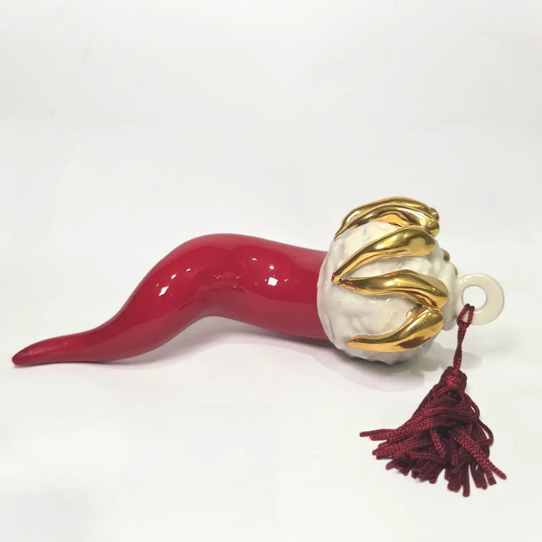 Corno portafortuna in ceramica rossa lucida di manifattura artigianale, caratterizzato da una punta ricurva e una corona regale dorata posta sulla sommità. Questo amuleto scaramantico dal design classico è un complemento d'arredo elegante, ideale come regalo di buon augurio o per decorare ambienti con un tocco di tradizione mediterranea.
