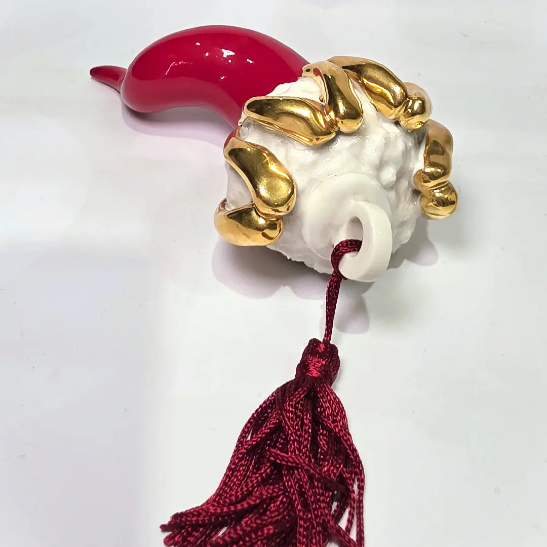 Corno portafortuna in ceramica rossa lucida di manifattura artigianale, caratterizzato da una punta ricurva e una corona regale dorata posta sulla sommità. Questo amuleto scaramantico dal design classico è un complemento d'arredo elegante, ideale come regalo di buon augurio o per decorare ambienti con un tocco di tradizione mediterranea.