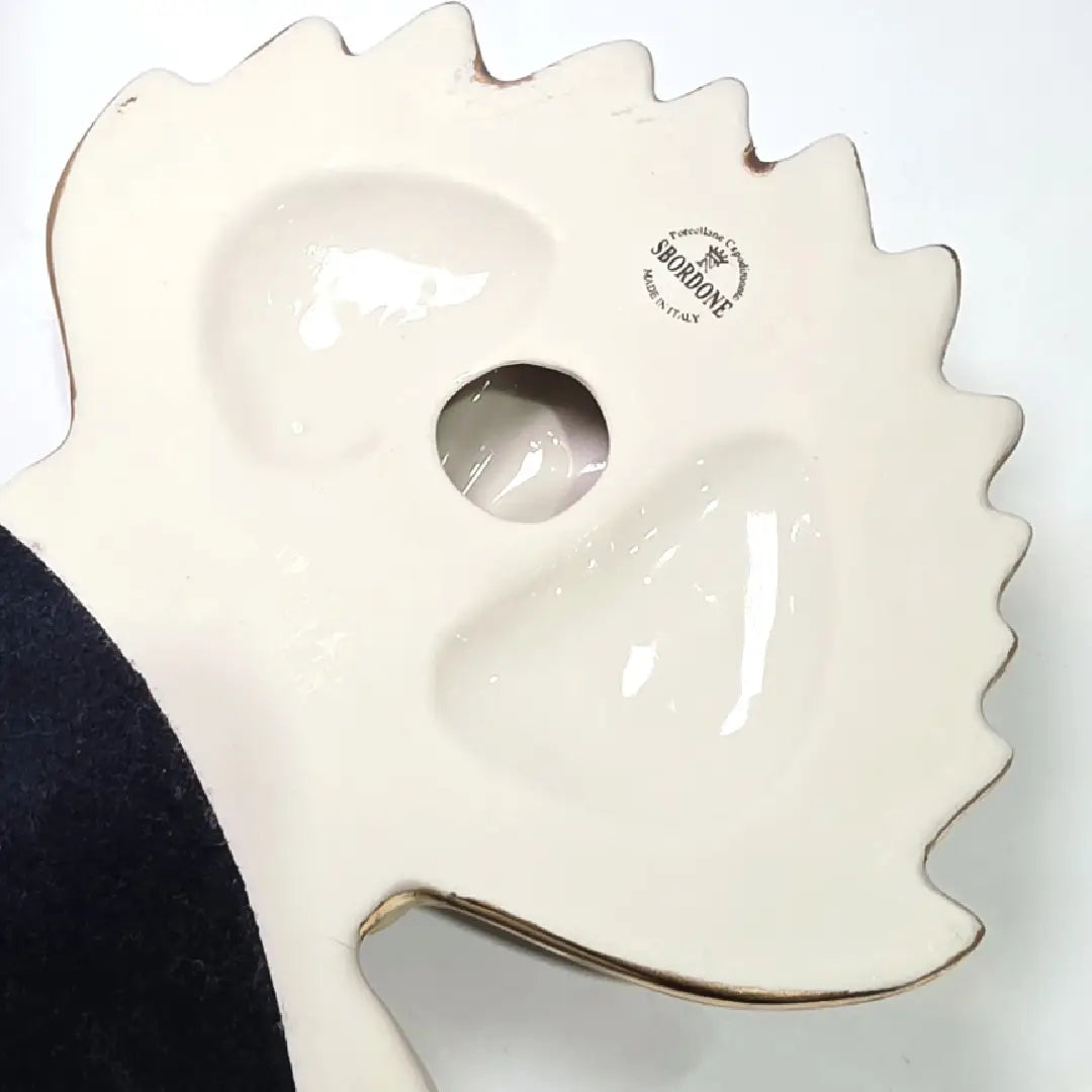 Scultura da parete a forma di Cuore Sacro grande in ceramica bianca lucida, decorata con molteplici loghi fashion neri e sormontata da una fiamma dorata finemente lavorata. L'oggetto presenta una cornice perlinata con borchie oro ed è un complemento d'arredo pop art di grande impatto visivo, ideale per personalizzare pareti in ambienti moderni e di lusso.