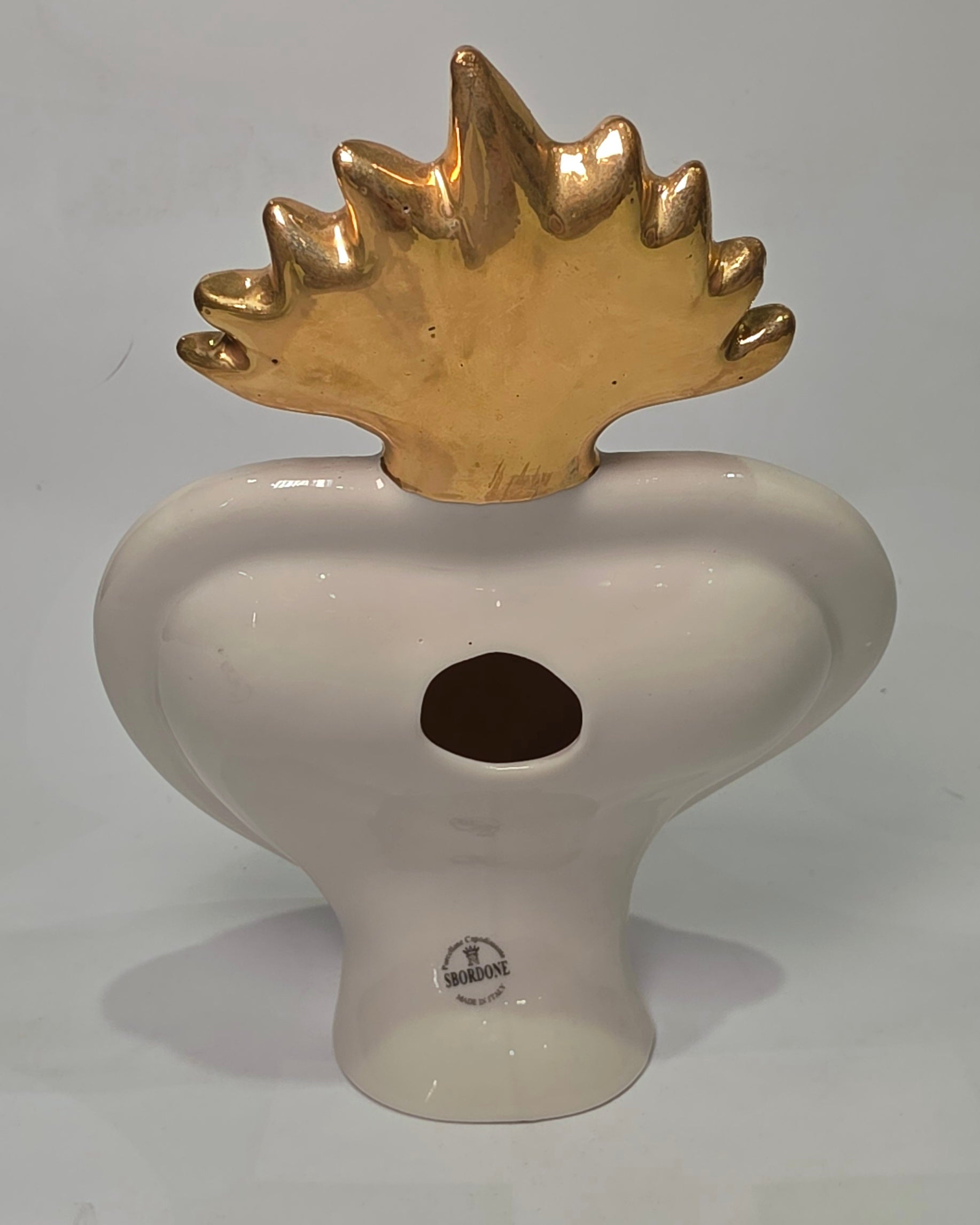 Scultura decorativa a forma di Cuore Sacro in ceramica bianca lucida, impreziosita da loghi fashion neri a contrasto e una maestosa fiamma superiore dorata. Questo complemento d'arredo di design presenta una cornice perlinata con borchie oro e una base d'appoggio, ideale per decorare ambienti moderni con un tocco pop art esclusivo.
