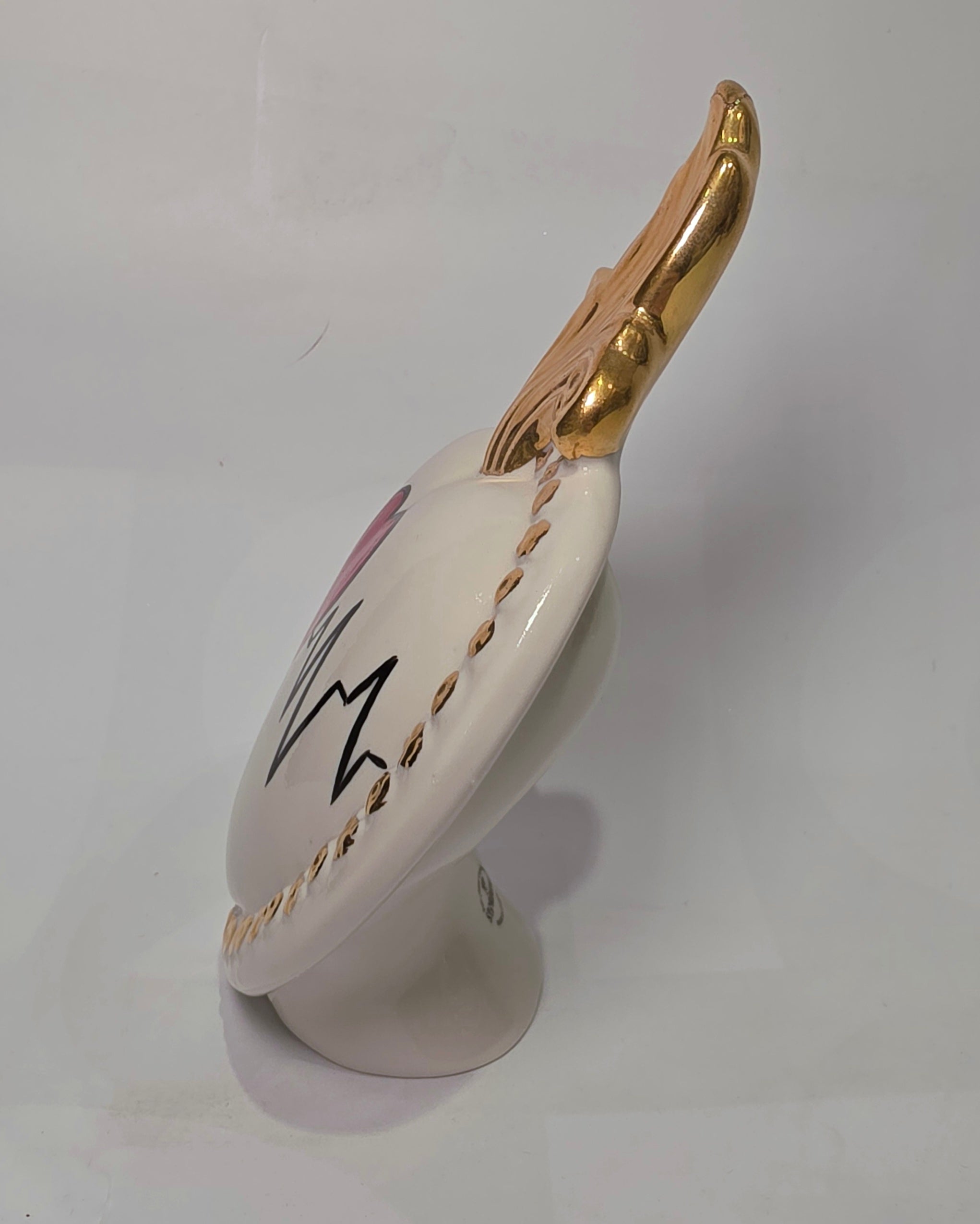 Scultura decorativa a forma di Cuore Sacro in ceramica bianca lucida, caratterizzata da un cuore rosso centrale sovrapposto a un disegno grafico nero che richiama il battito cardiaco. L'oggetto è impreziosito da una fiamma superiore dorata e una cornice perlinata con borchie oro, rendendolo un complemento d'arredo dal design moderno e originale.