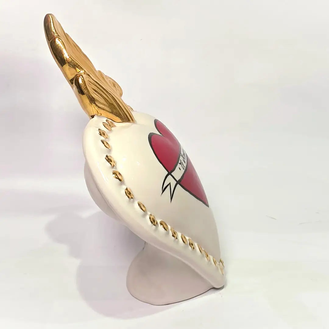 Scultura decorativa a forma di Cuore Sacro in ceramica bianca lucida, decorata al centro con un cuore rosso e una pergamena con la scritta "Ti Amo". L'oggetto è impreziosito da una fiamma superiore dorata e una cornice perlinata con borchie oro, rappresentando un'idea regalo romantica e un complemento d'arredo dal design unico.