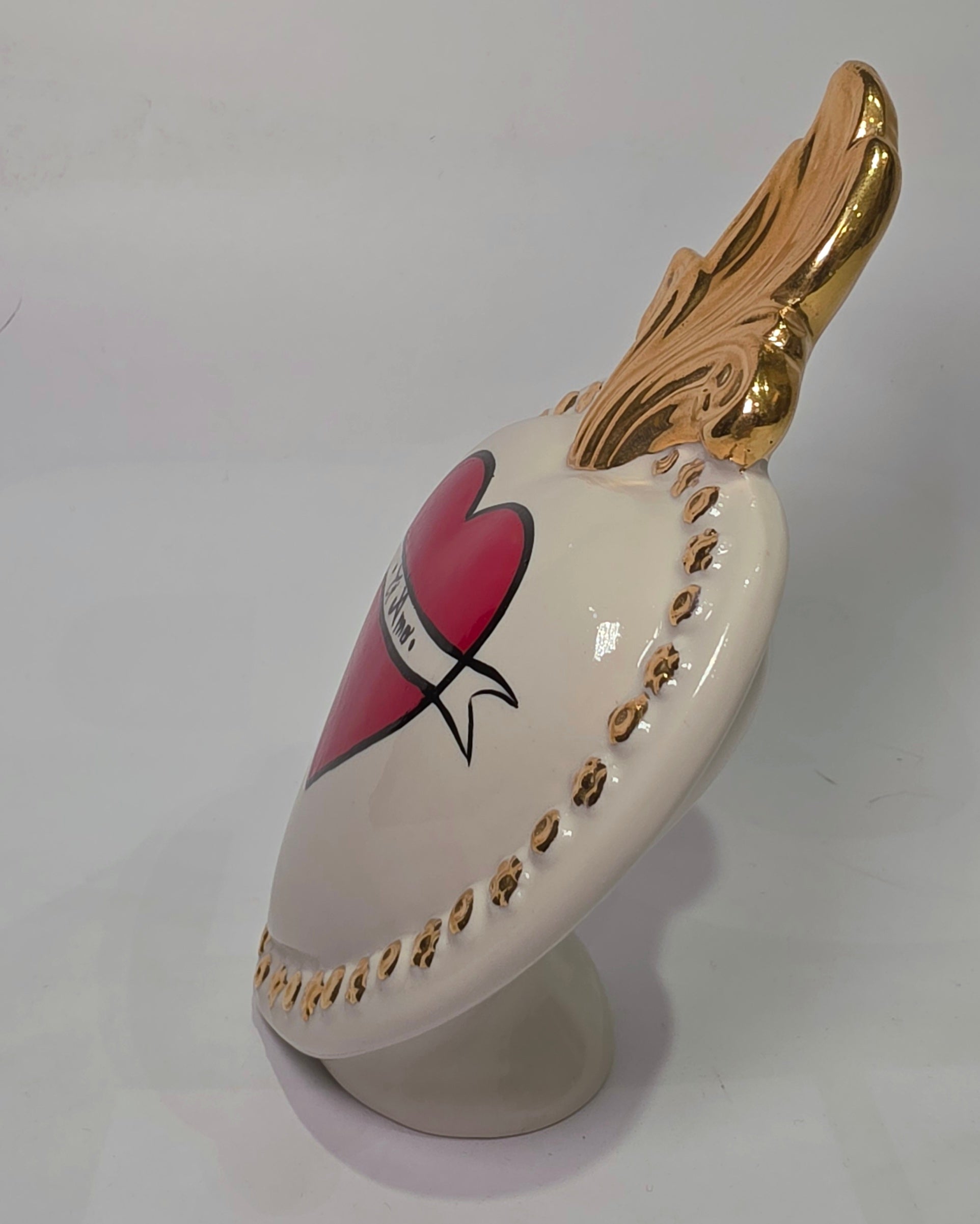 Scultura decorativa a forma di Cuore Sacro in ceramica bianca lucida, decorata al centro con un cuore rosso e una pergamena con la scritta "Ti Amo". L'oggetto è impreziosito da una fiamma superiore dorata e una cornice perlinata con borchie oro, rappresentando un'idea regalo romantica e un complemento d'arredo dal design unico.