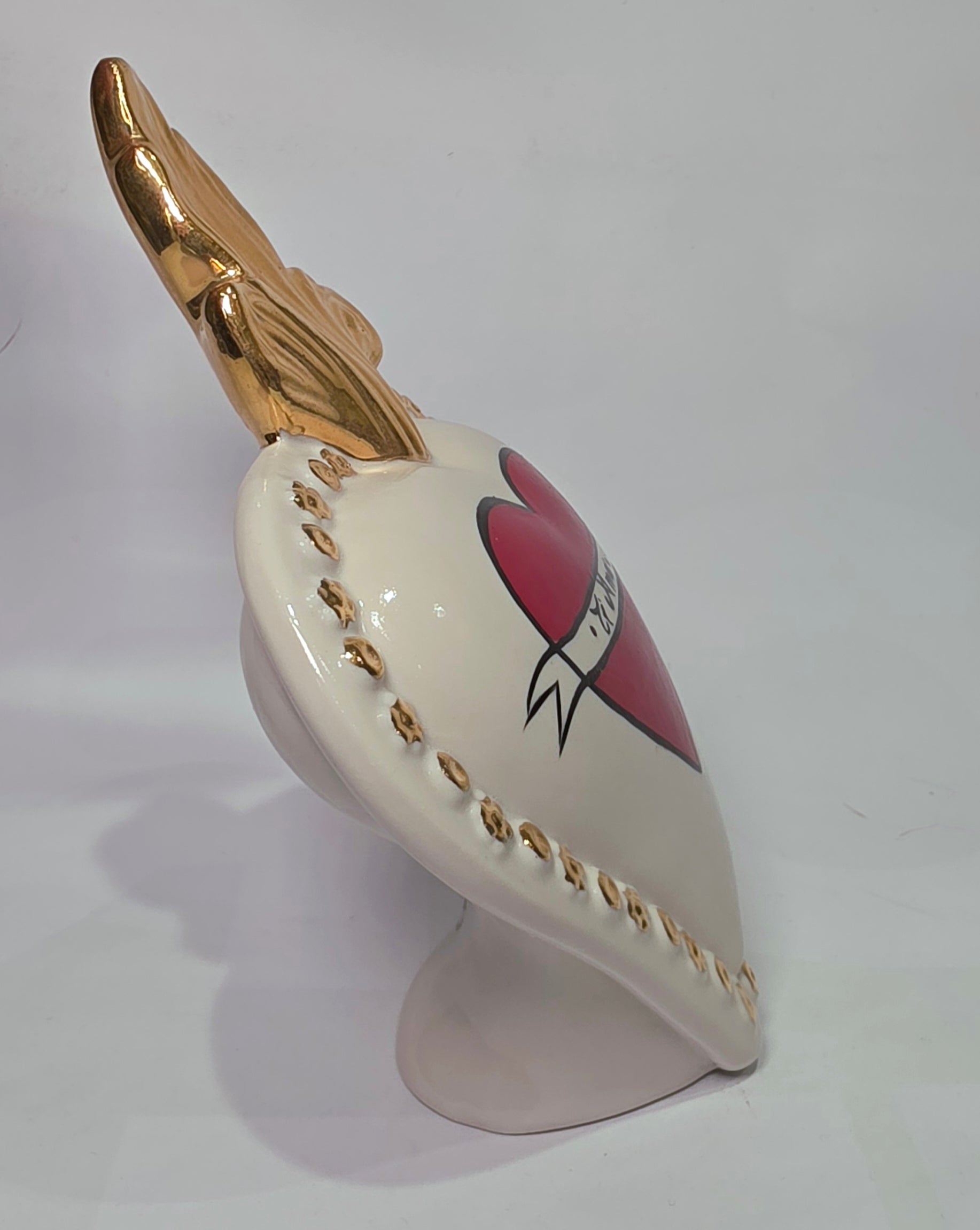Scultura decorativa a forma di Cuore Sacro in ceramica bianca lucida, decorata al centro con un cuore rosso e una pergamena con la scritta "Ti Amo". L'oggetto è impreziosito da una fiamma superiore dorata e una cornice perlinata con borchie oro, rappresentando un'idea regalo romantica e un complemento d'arredo dal design unico.