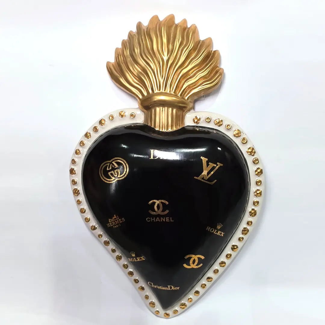 Scultura da parete a forma di Cuore Sacro grande in ceramica nera lucida, impreziosita da numerosi loghi fashion dorati e sormontata da una fiamma in oro finemente scolpita. Questo complemento d'arredo pop art presenta una cornice bianca perlinata con borchie oro, perfetto per decorare con lusso e originalità gli interni di una casa moderna.