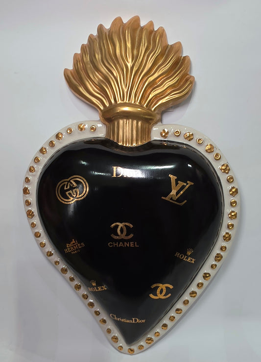 Scultura da parete a forma di Cuore Sacro grande in ceramica nera lucida, impreziosita da numerosi loghi fashion dorati e sormontata da una fiamma in oro finemente scolpita. Questo complemento d'arredo pop art presenta una cornice bianca perlinata con borchie oro, perfetto per decorare con lusso e originalità gli interni di una casa moderna.