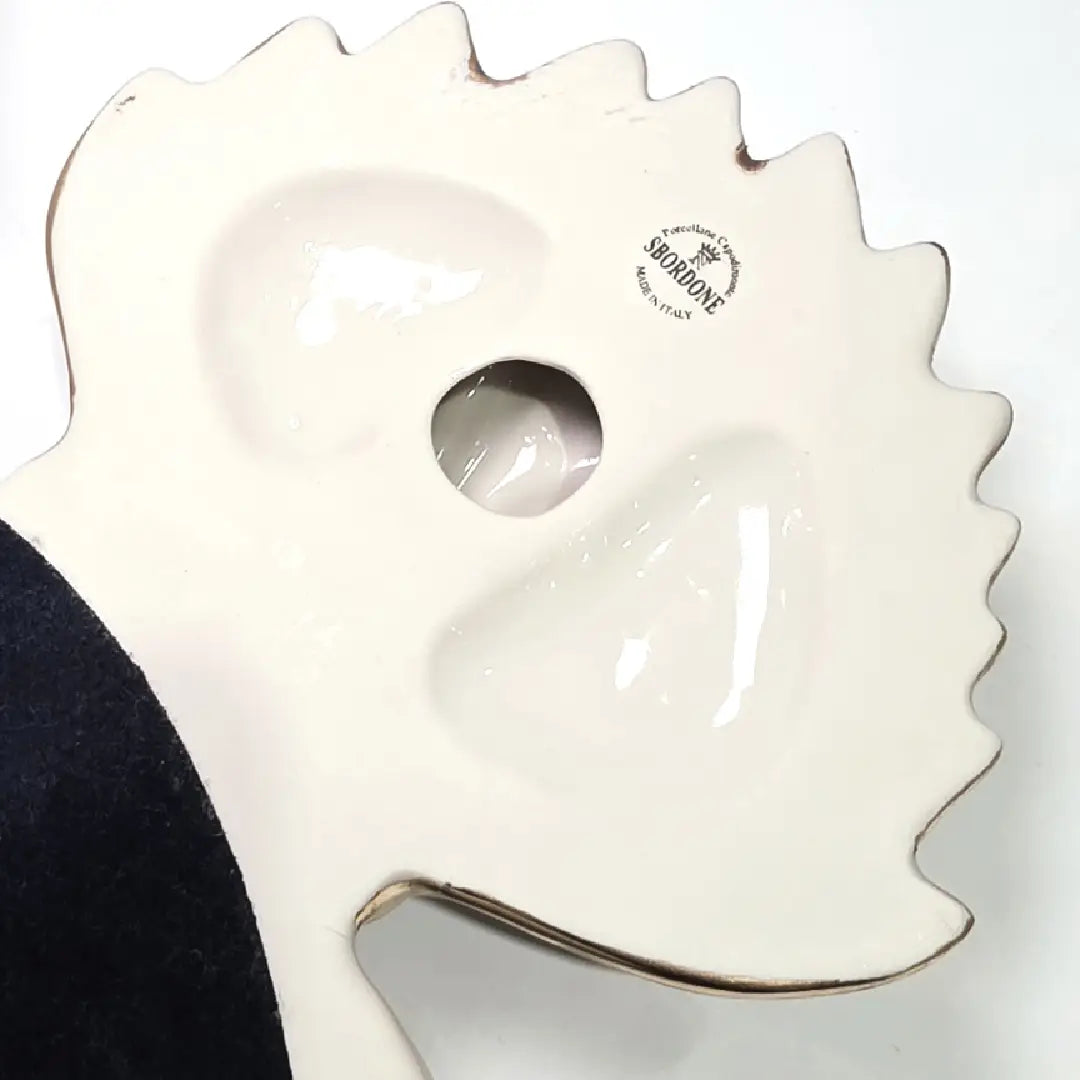 Scultura da parete a forma di Cuore Sacro grande in ceramica nera lucida, impreziosita da numerosi loghi fashion dorati e sormontata da una fiamma in oro finemente scolpita. Questo complemento d'arredo pop art presenta una cornice bianca perlinata con borchie oro, perfetto per decorare con lusso e originalità gli interni di una casa moderna.